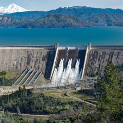 Picture of Shasta Dam surrounded by roads and trees with a lake and mountains on the background A picture of Shasta Dam surrounded by roads and trees with a lake and mountains on the background